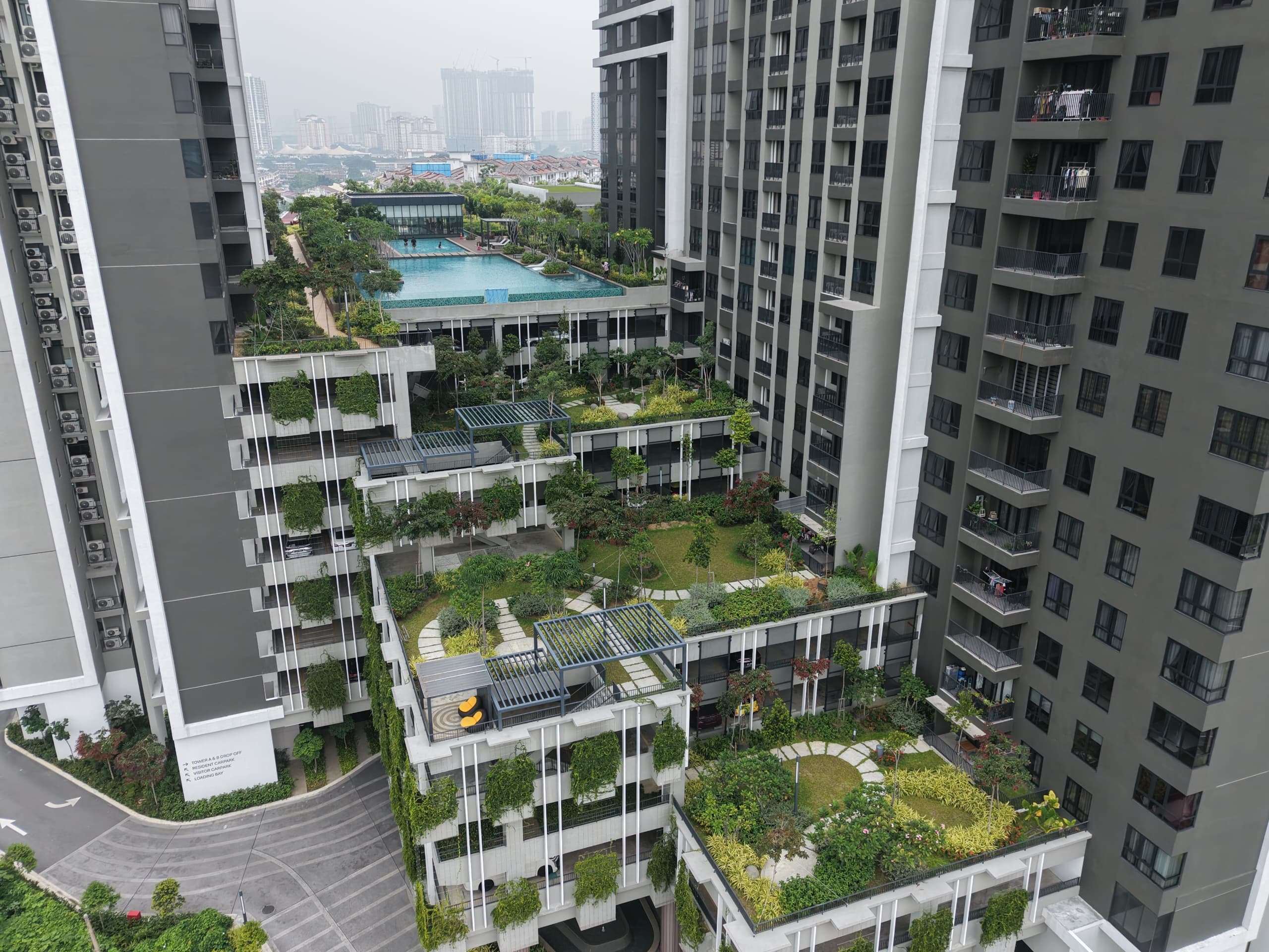 Elevated view of landscaped terraces, pergolas, and a turquoise swimming pool between apartment towers.