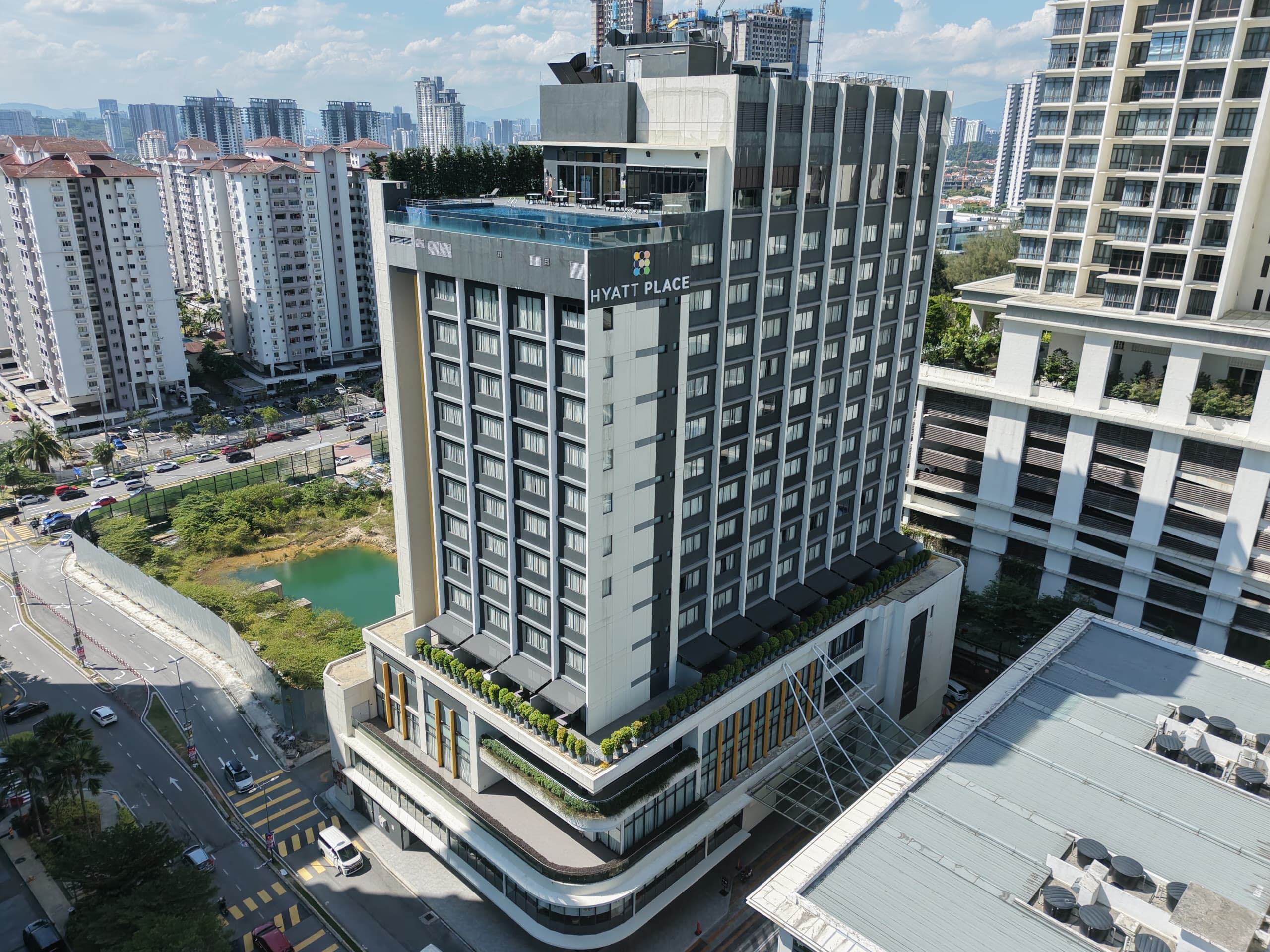 Aerial view of Hyatt Place building with grey facade, rooftop pool, and planted podium terraces.