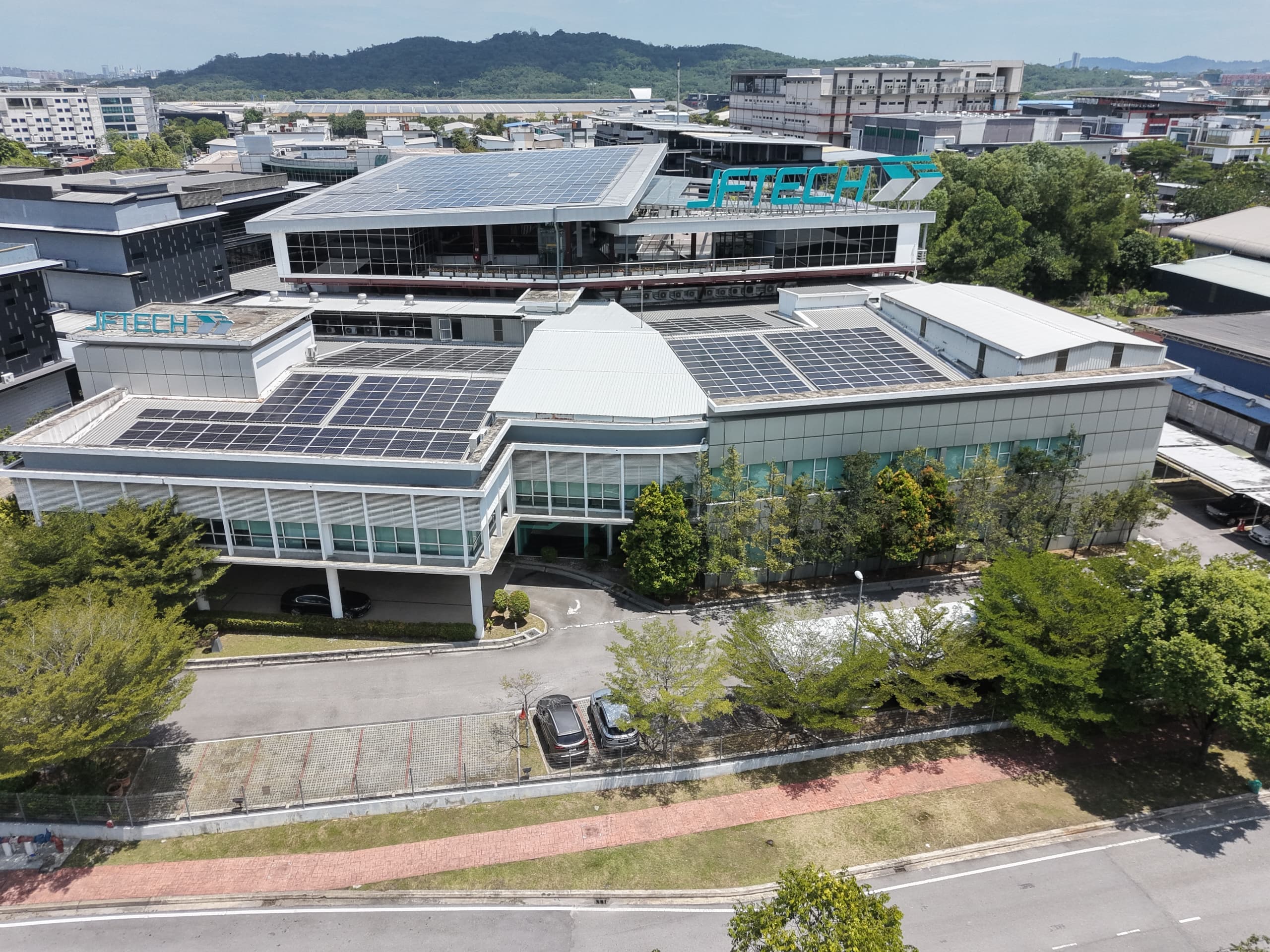 Aerial view of a low-rise commercial building with solar-panel roofs, glazed facades, and visible JFTECH signage.