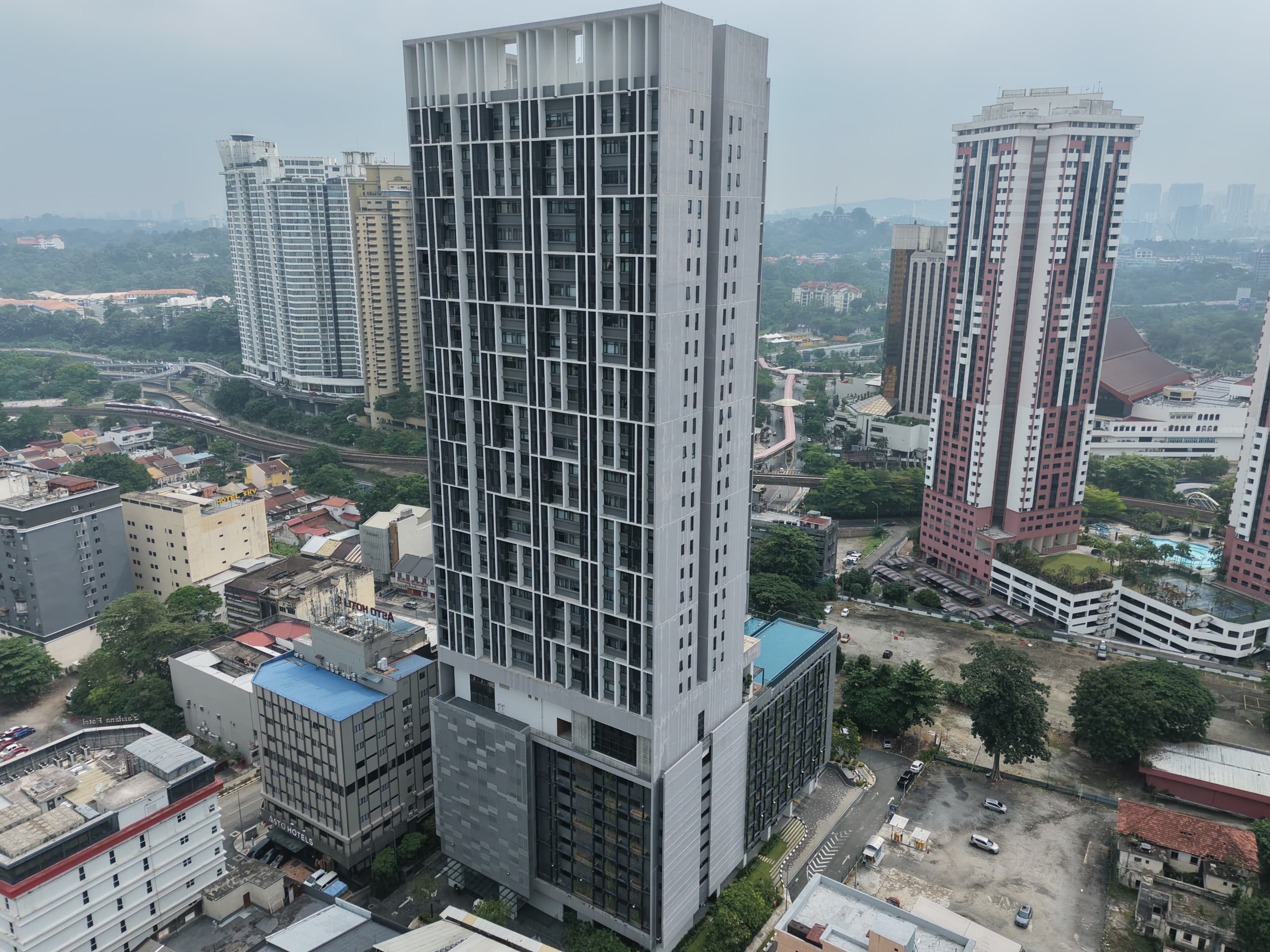 Aerial view of a tall grey residential tower with gridded facade above dense city blocks.